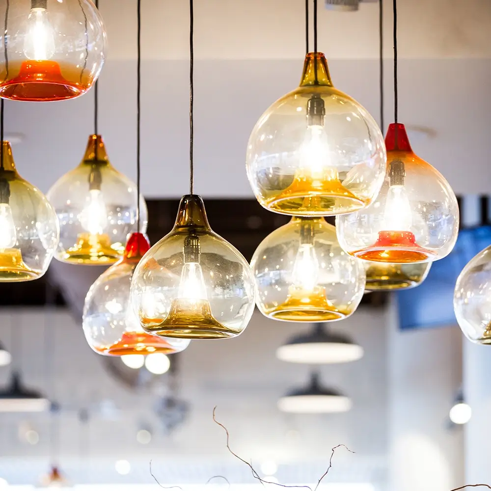 Several modern glass pendant lights with gold and red accents hang from the ceiling, glowing warmly—an inviting ambiance perfect for stylish spaces that think healthcare. The background reveals a blurred interior with more lights and contemporary decor.